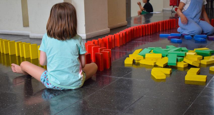 NIña de espaldas sentada en el suelo jugando con maderas de colores.