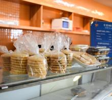 Fotografía de la cantina. En primer plano varias bolsas con galletitas y bandejas de alfajores sobre una vitrina. Desenfocado se ve también sobre la vitrina una lista de precios en fondo azul sobre letras blancas con título Combos de café.